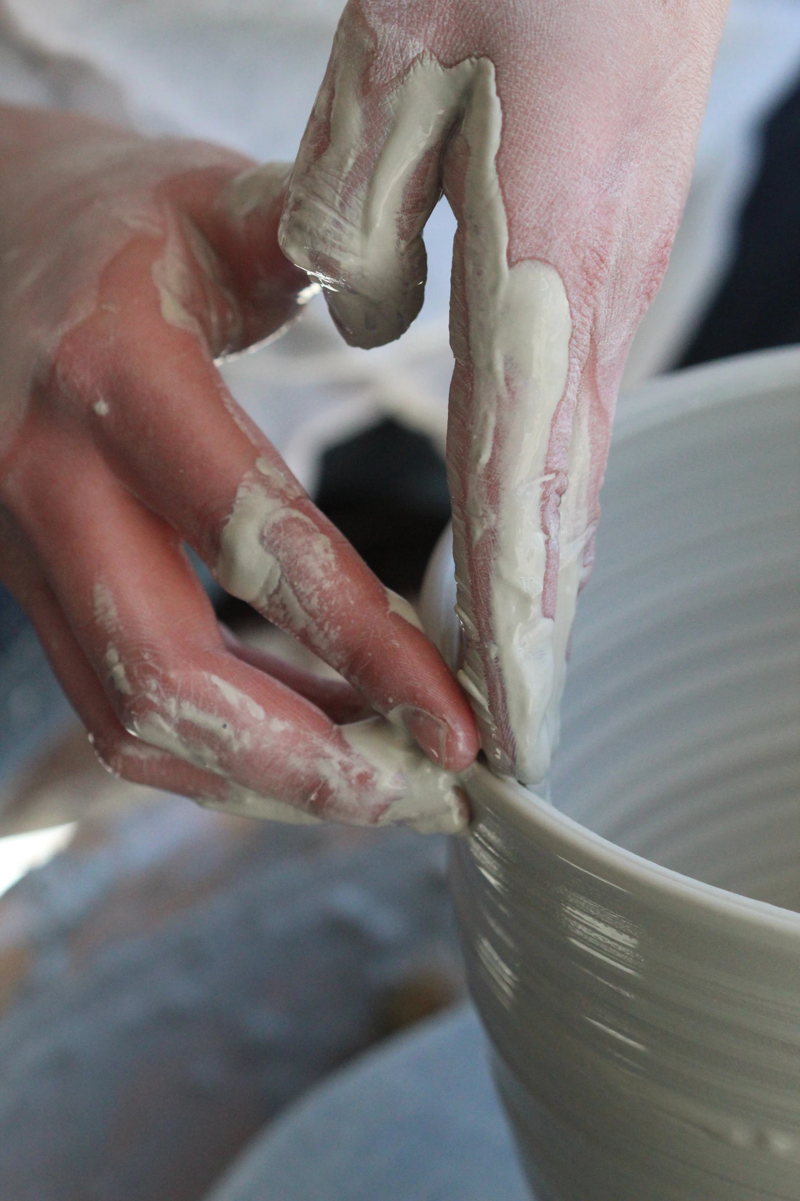 Hands shaping the rim of a clay bowl